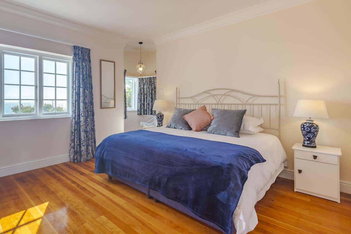 Un dormitorio con una cama grande, una mesita de noche con lámpara, una ventana con cortinas y vistas al exterior.