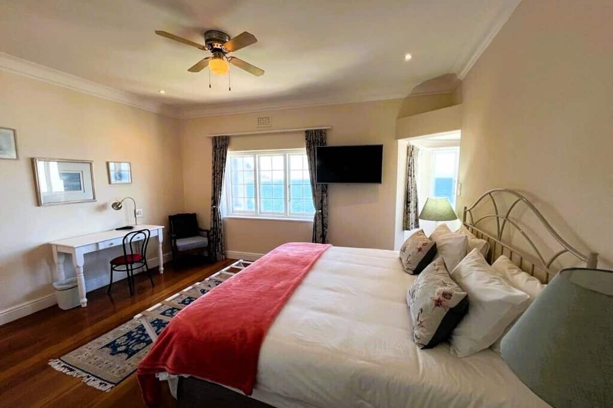 Un dormitorio con cama, escritorio, silla, televisor y ventana con cortinas.