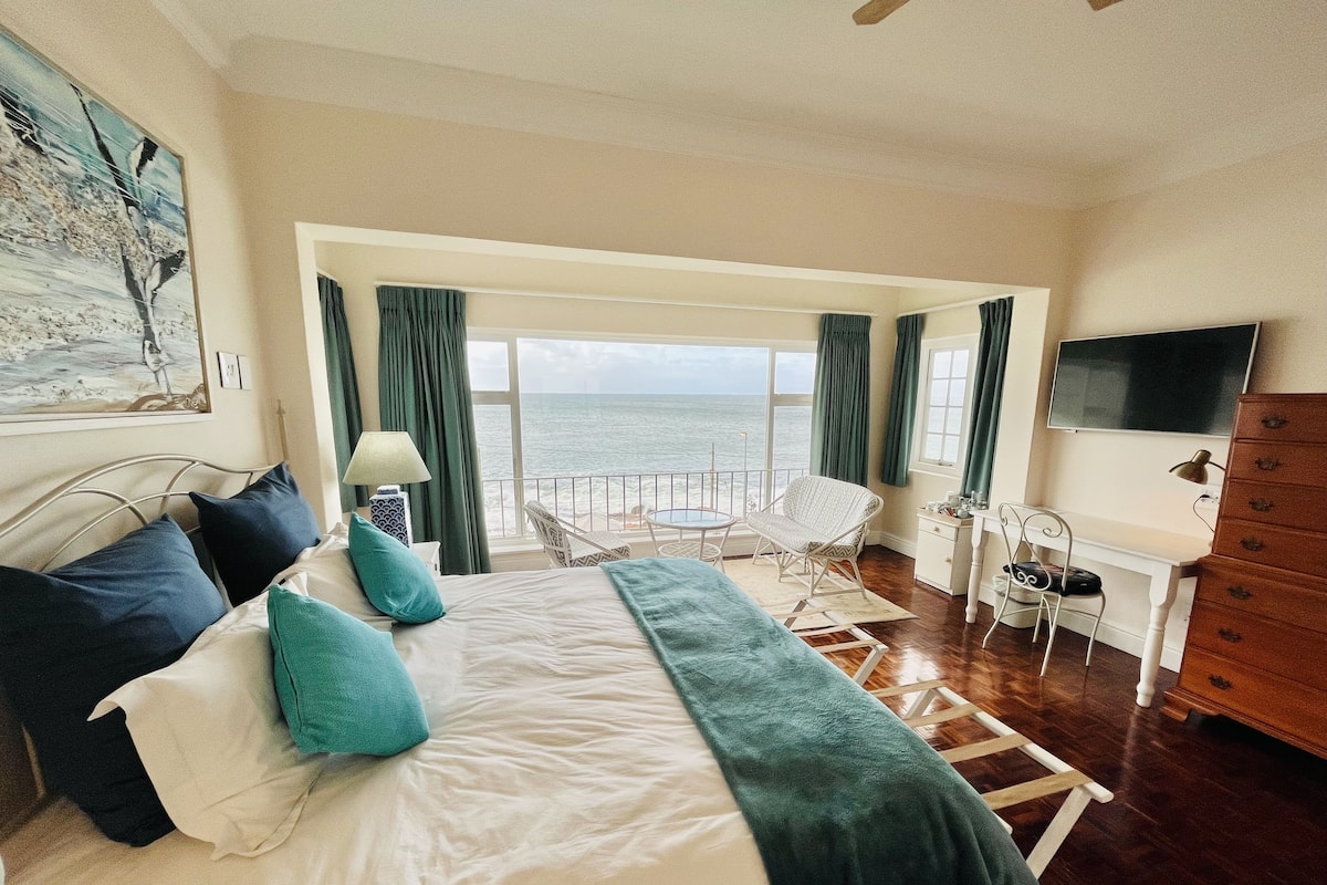Un dormitorio con cama, escritorio, silla y vista al mar.
