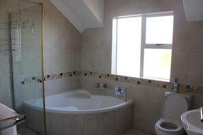 A bathroom with a glass-enclosed shower, a freestanding bathtub, a toilet, and a window providing natural light.