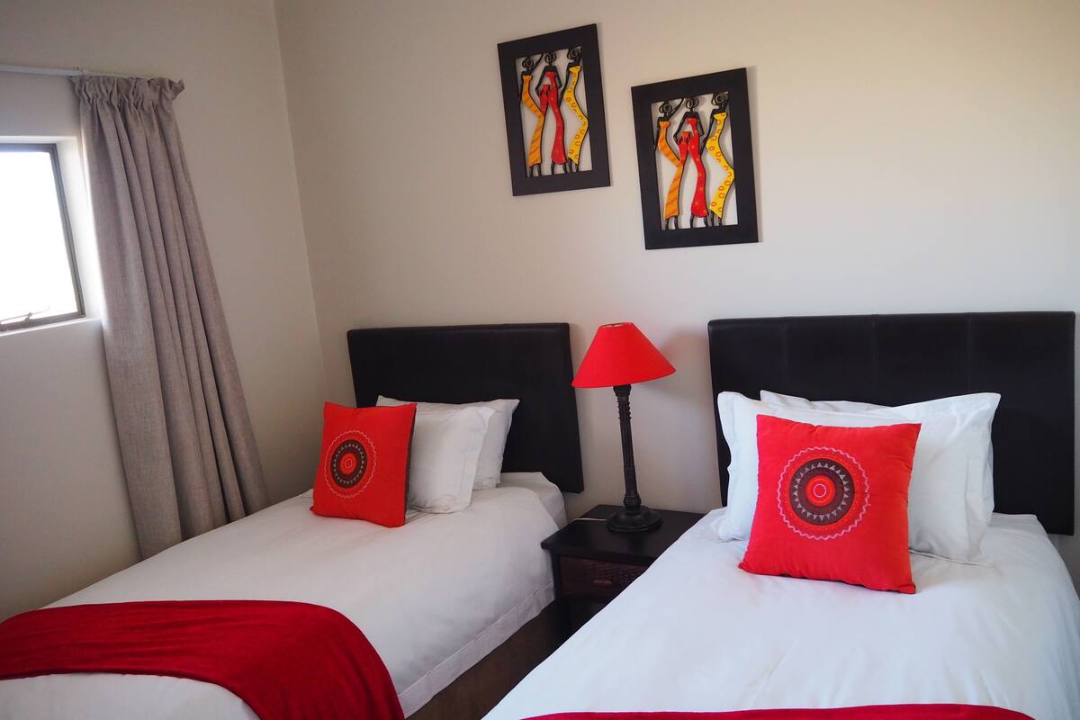 Habitación de hotel con dos camas, cada una con una almohada roja y una mesita de noche negra con una lámpara roja.