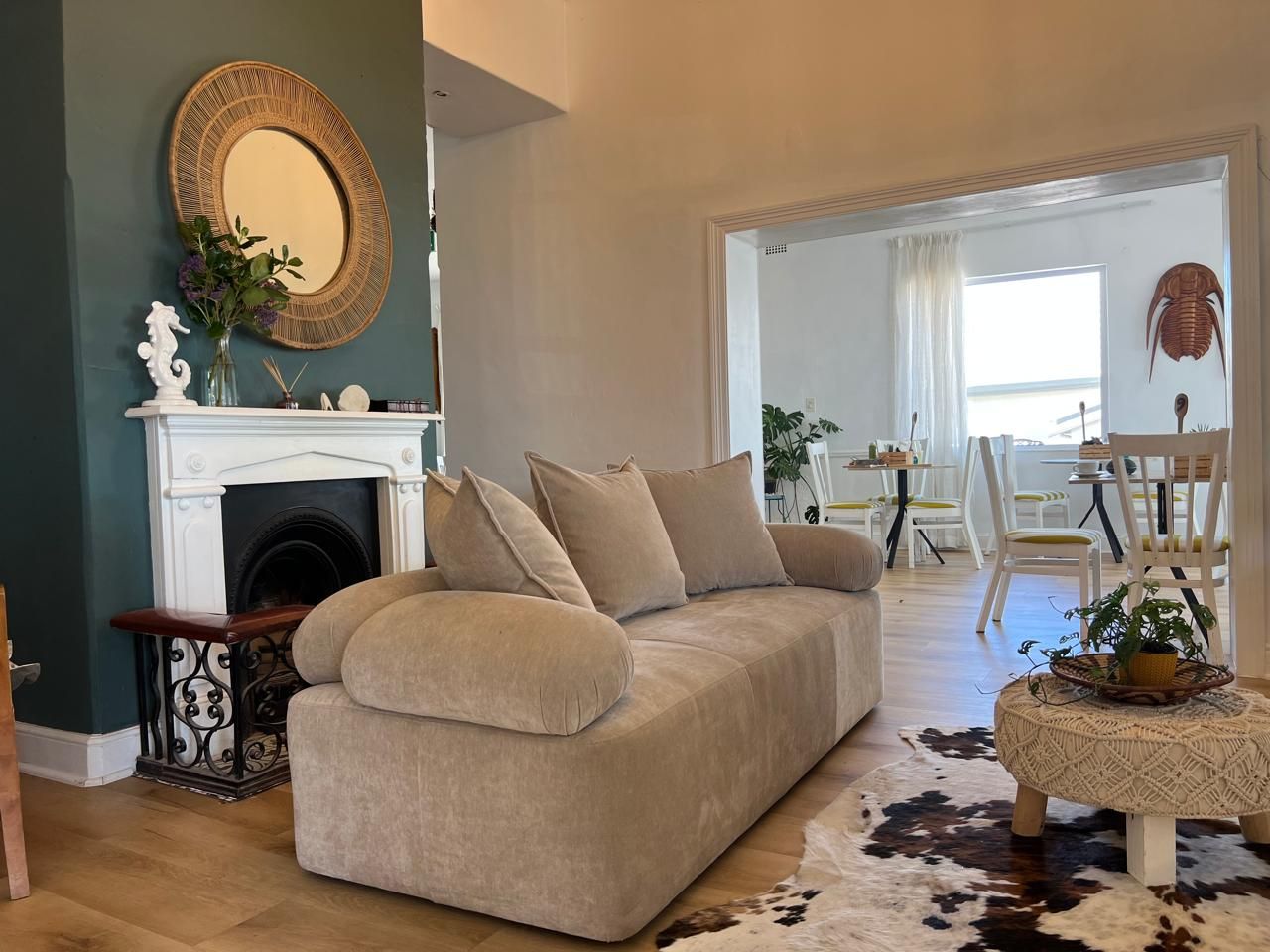 A living room with a beige sofa, a fireplace, a cowhide rug, and a dining area in the background.
