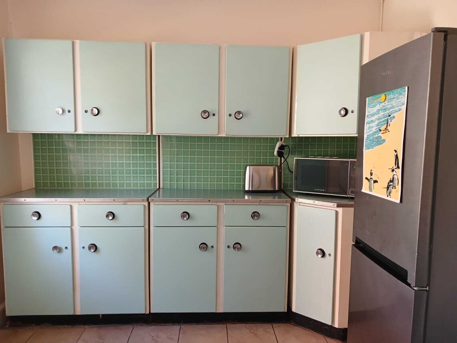 A kitchen with light blue cabinets, a green tiled backsplash, a toaster, a microwave, and a refrigerator with a beach scene on the door.