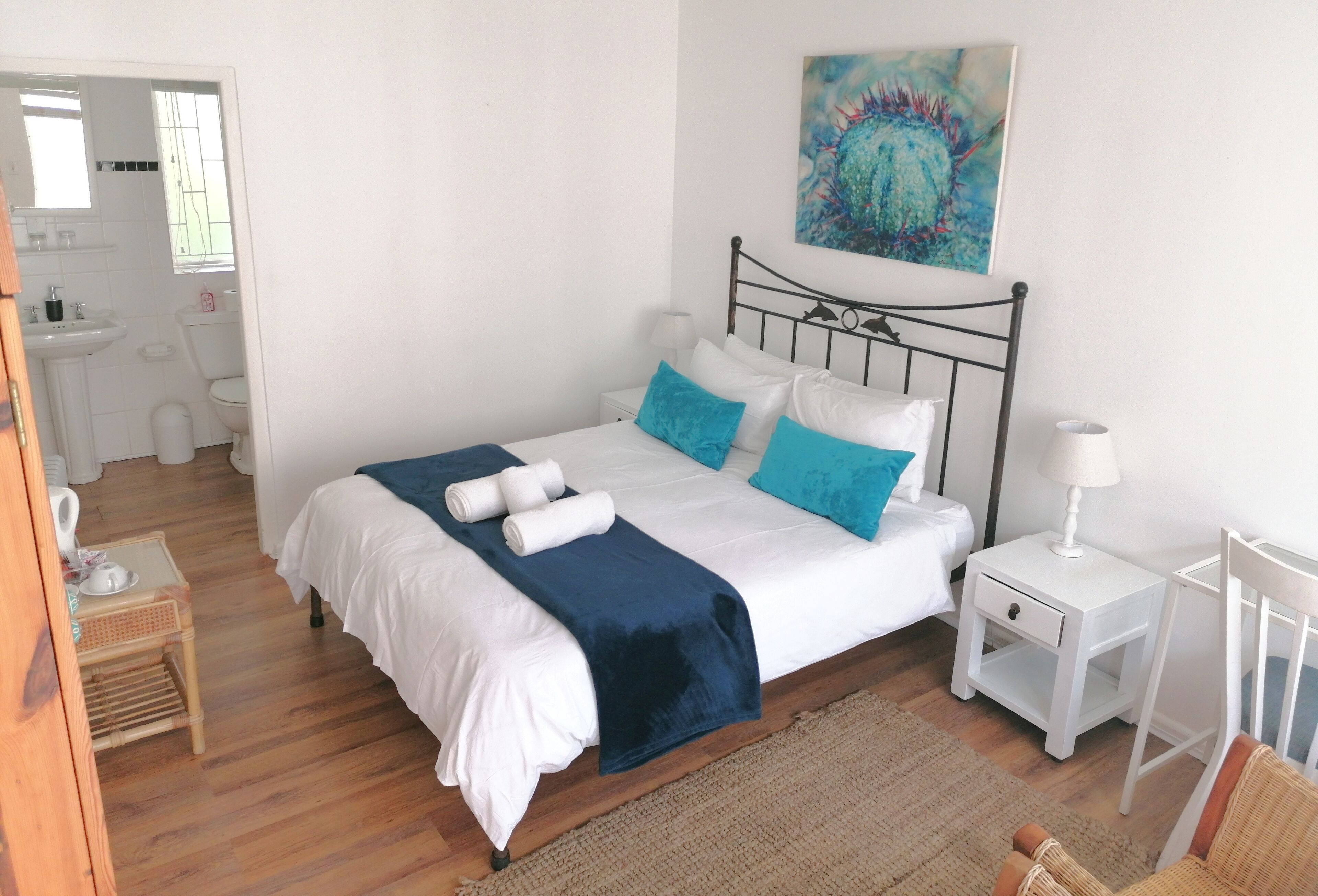 A neatly arranged bedroom with a bed, bedside tables, a nightstand, a chair, and a bathroom visible in the background.