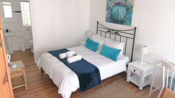 Une chambre à coucher bien rangée, avec un lit, des tables de chevet, une commode, une chaise, et une salle de bain visible au fond.
