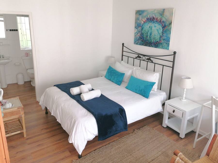 Une chambre à coucher bien rangée, avec un lit, des tables de chevet, une commode, une chaise, et une salle de bain visible au fond.