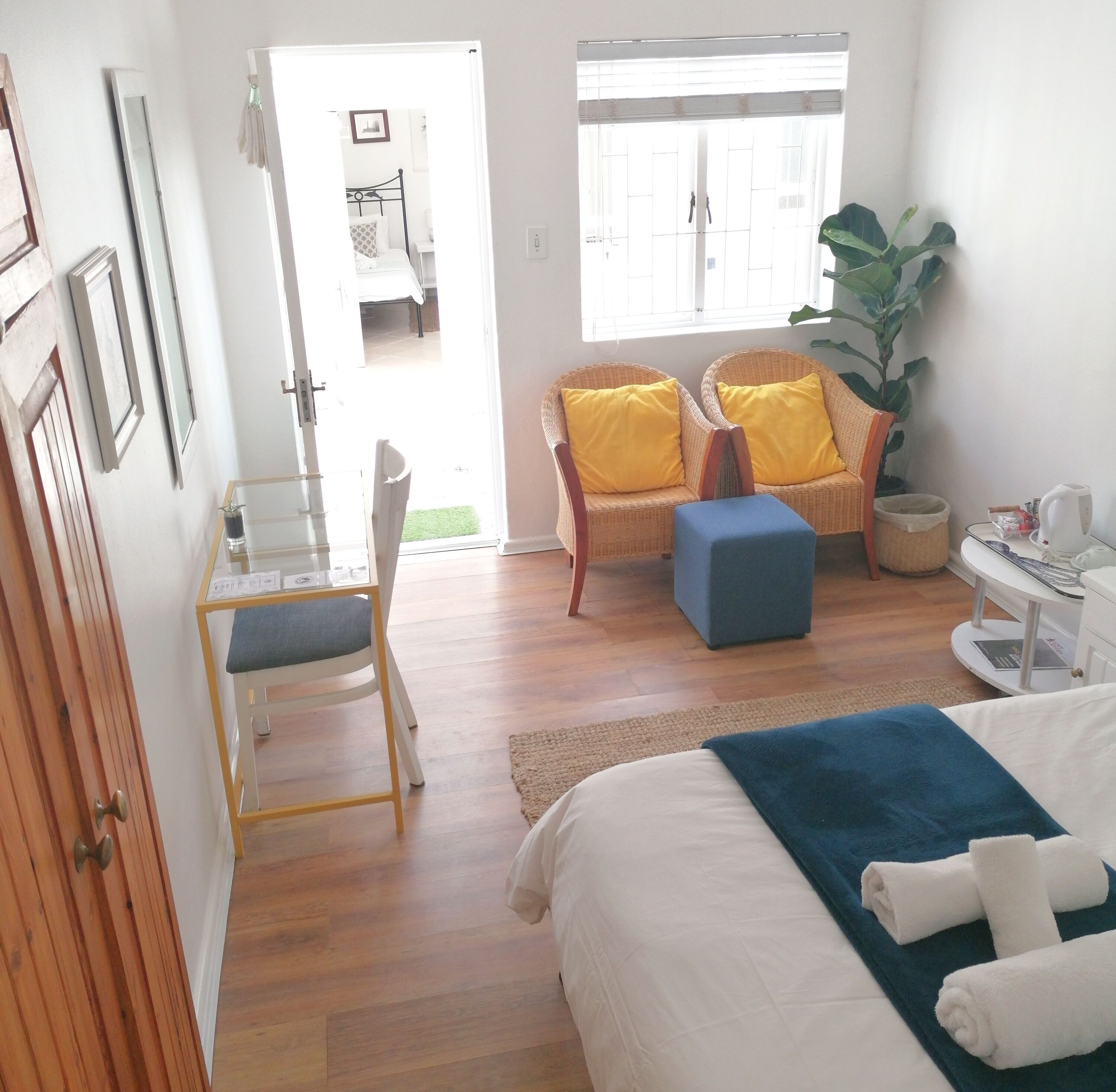 A bedroom with a bed, a desk, a chair, two armchairs, a window, and a plant.