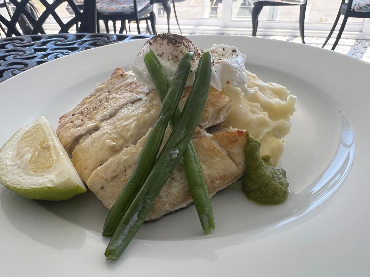 A plate with a piece of grilled fish, green beans, mashed potatoes, and a slice of lime.