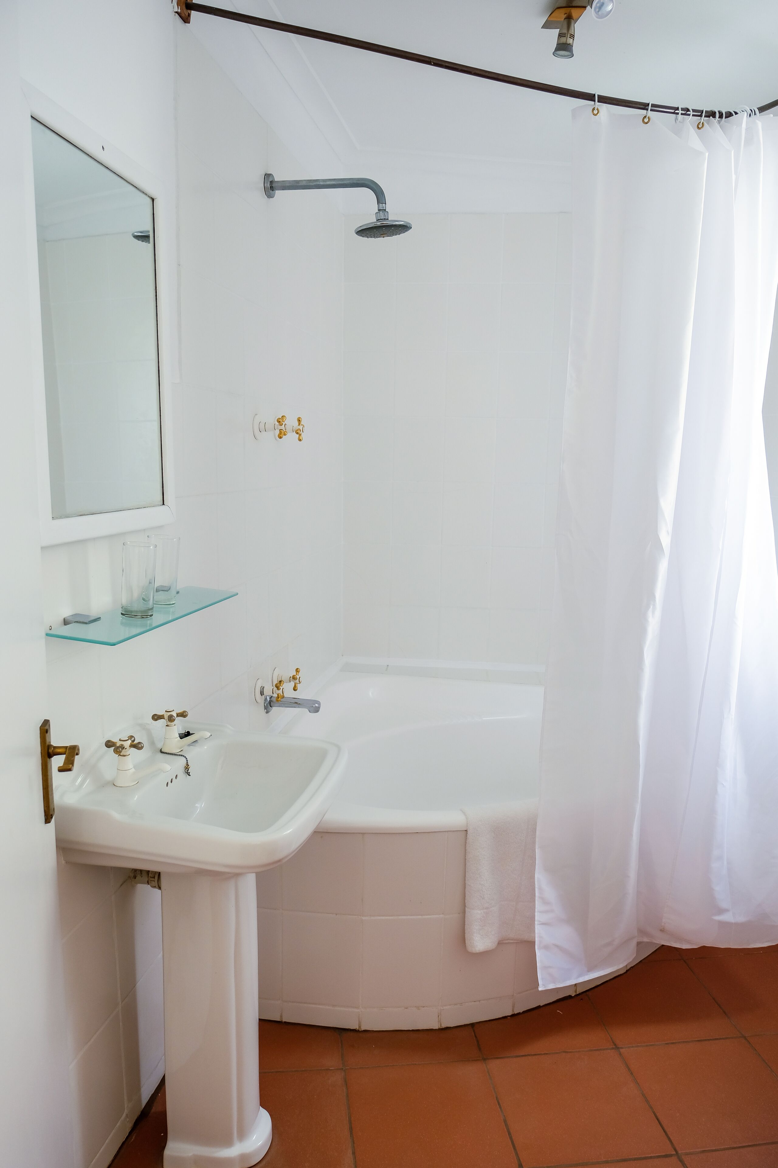 A bathroom with a white sink, a bathtub, a shower curtain, and a glass shelf.