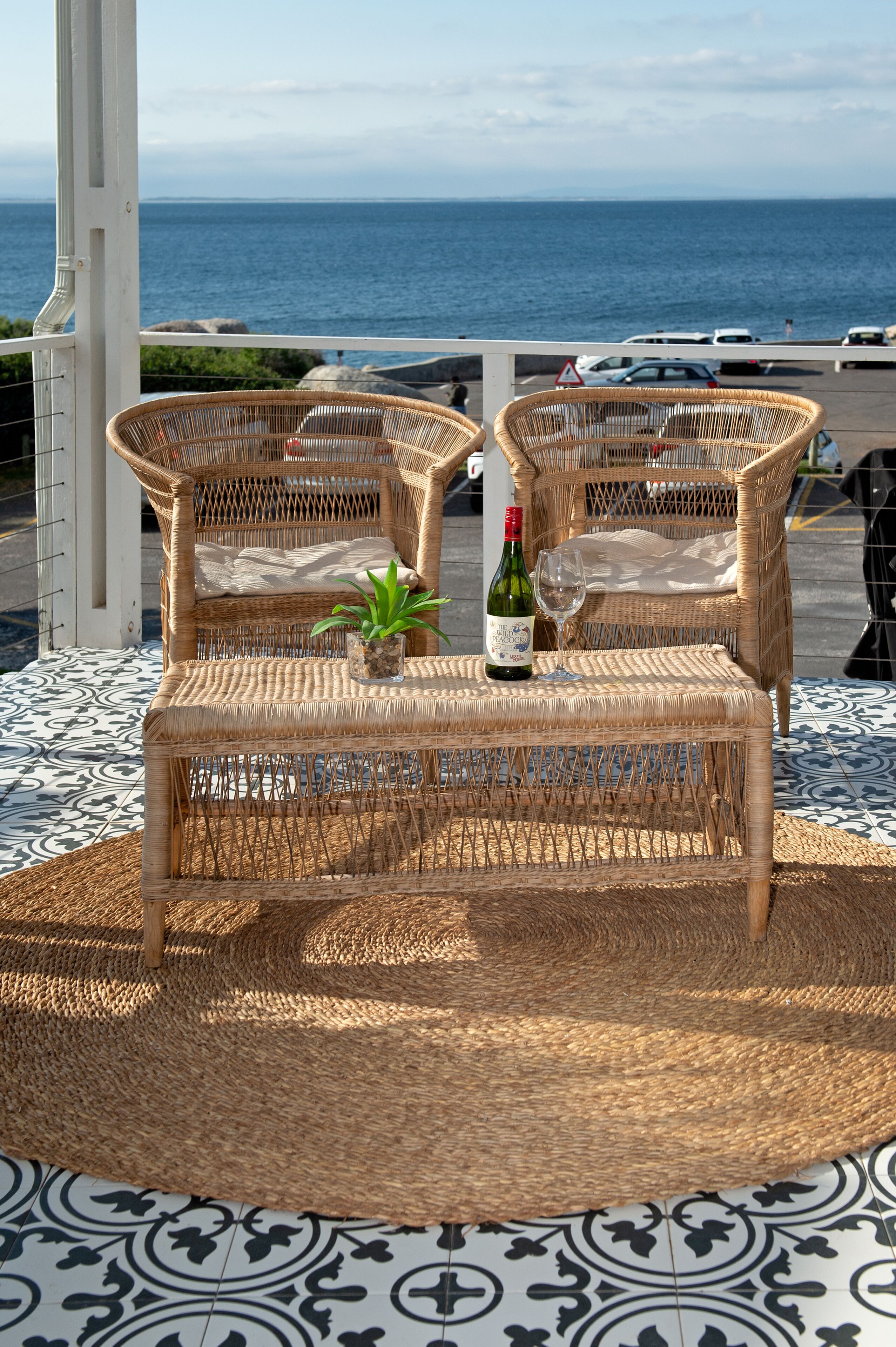 A wicker table with a bottle and glass, two wicker chairs, and a view of the sea.