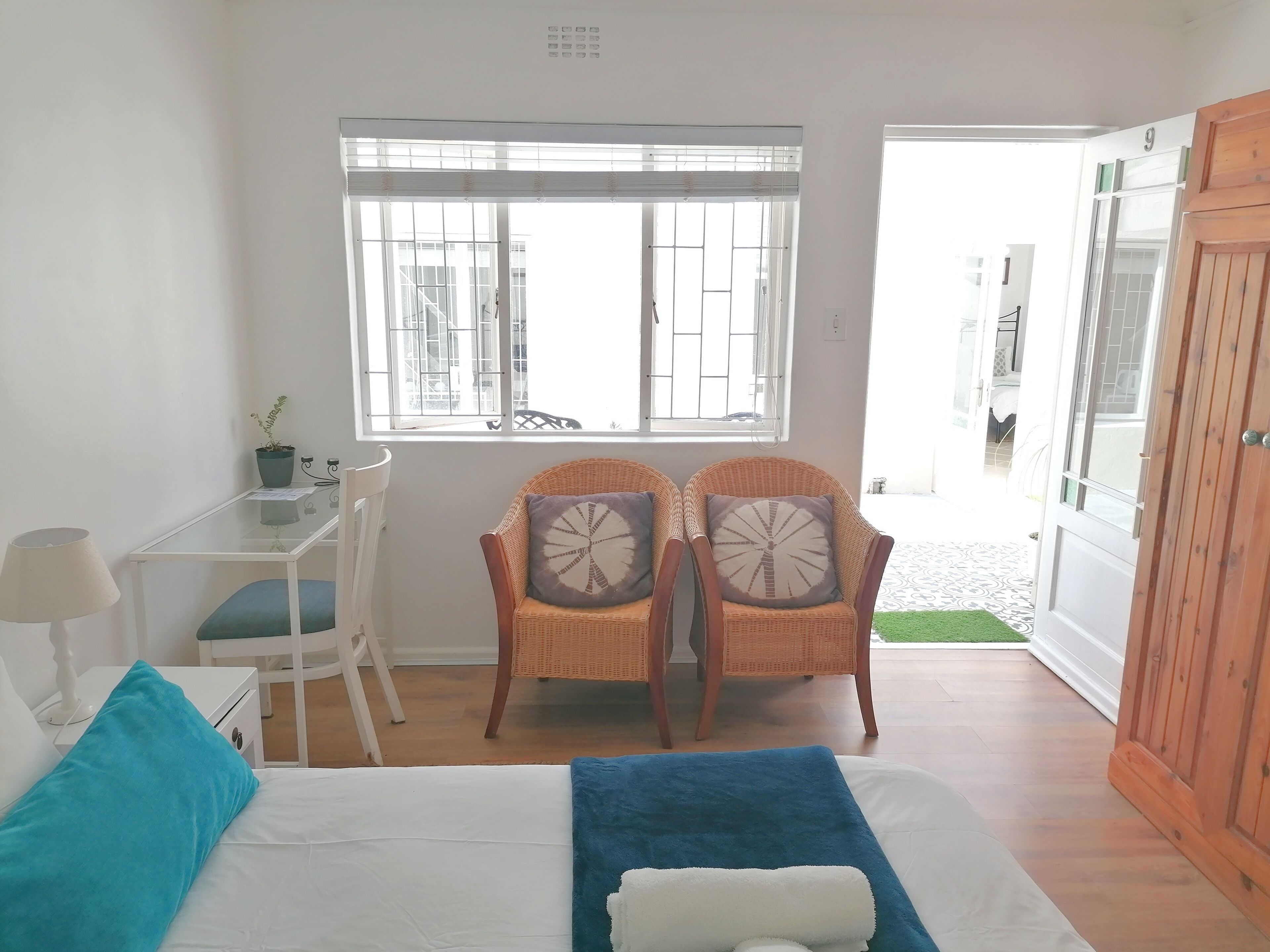 A room with a bed, a desk, two wicker chairs, a window, and a wooden wardrobe.