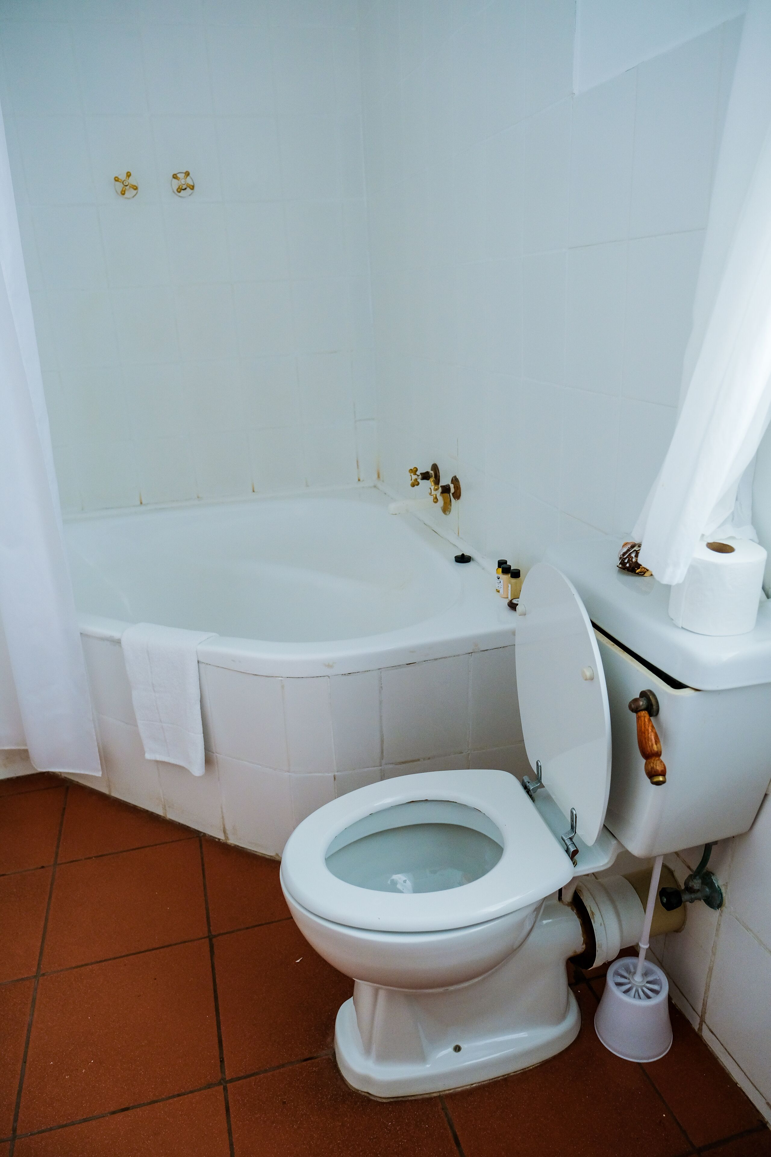 Et badeværelse med et hvidt badekar, et hvidt toilet og en hvid toiletpapirsholder.