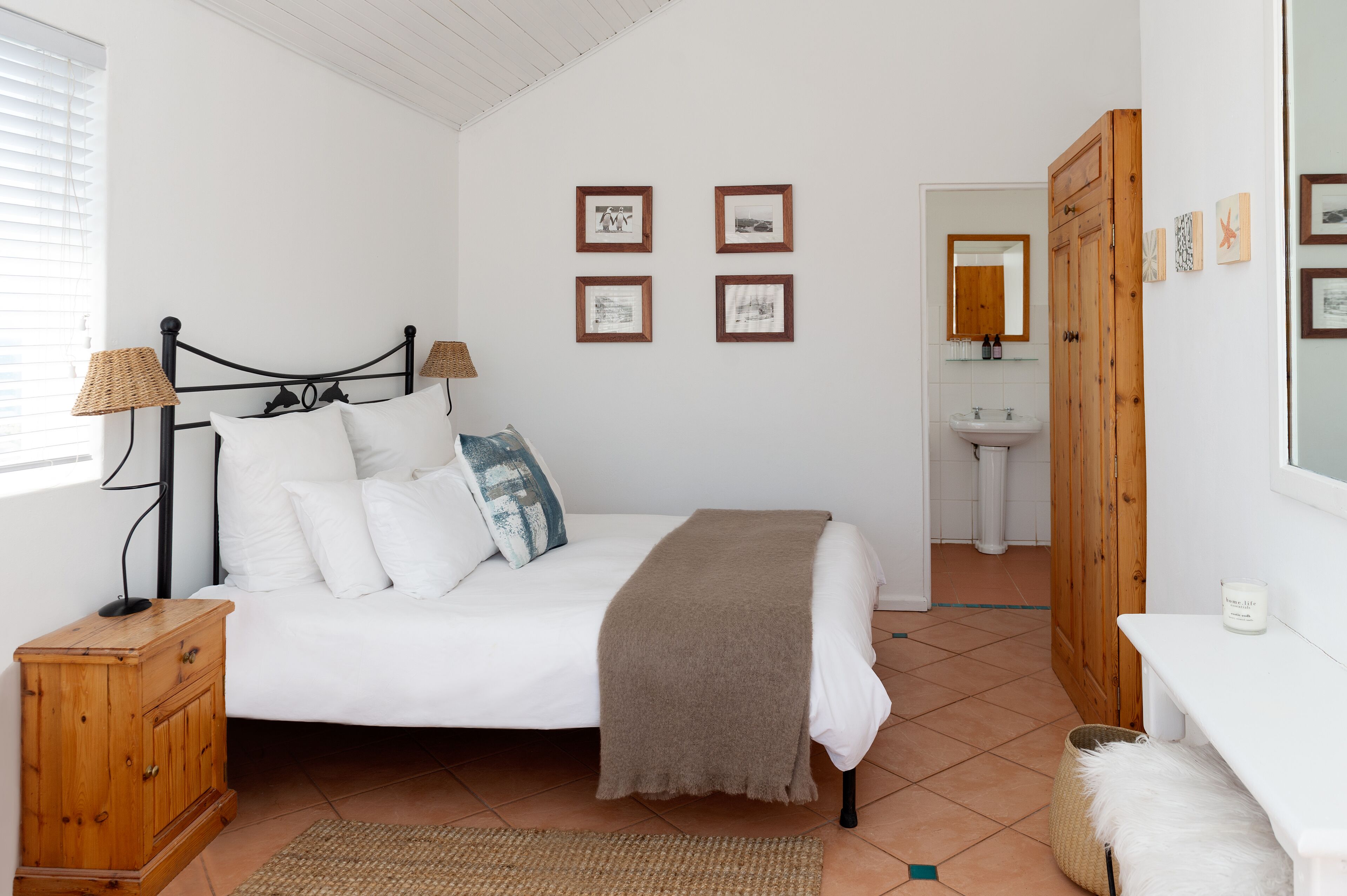 Un dormitorio con cama, lámparas de noche, una mesita de noche de madera y una pared con cuadros enmarcados.