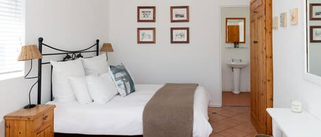 Un dormitorio con cama, lámparas de noche, una mesita de noche de madera y una pared con cuadros enmarcados.
