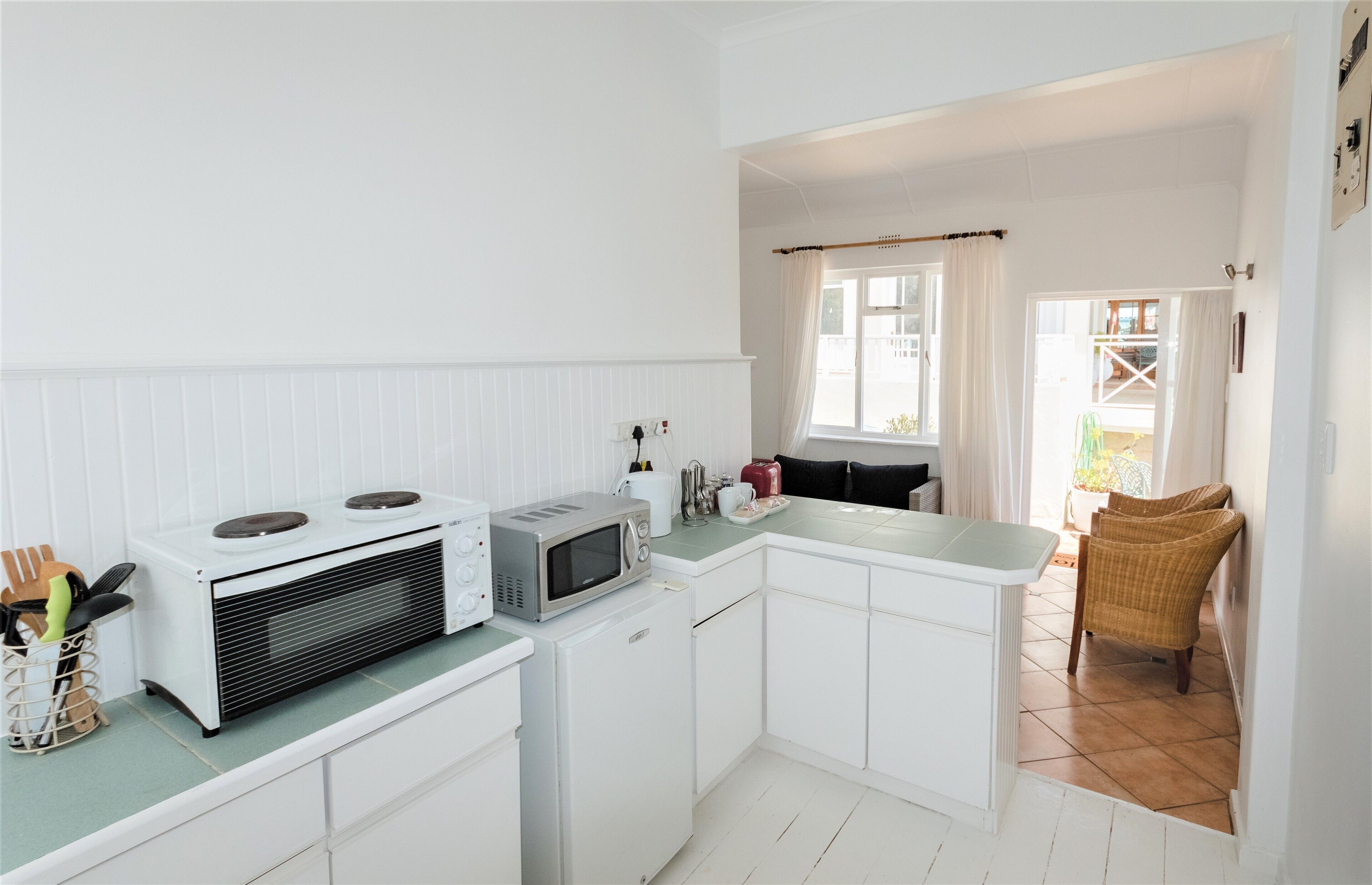 Uma cozinha compacta com armários brancos, micro-ondas, mini-geladeira e janela com cortinas.