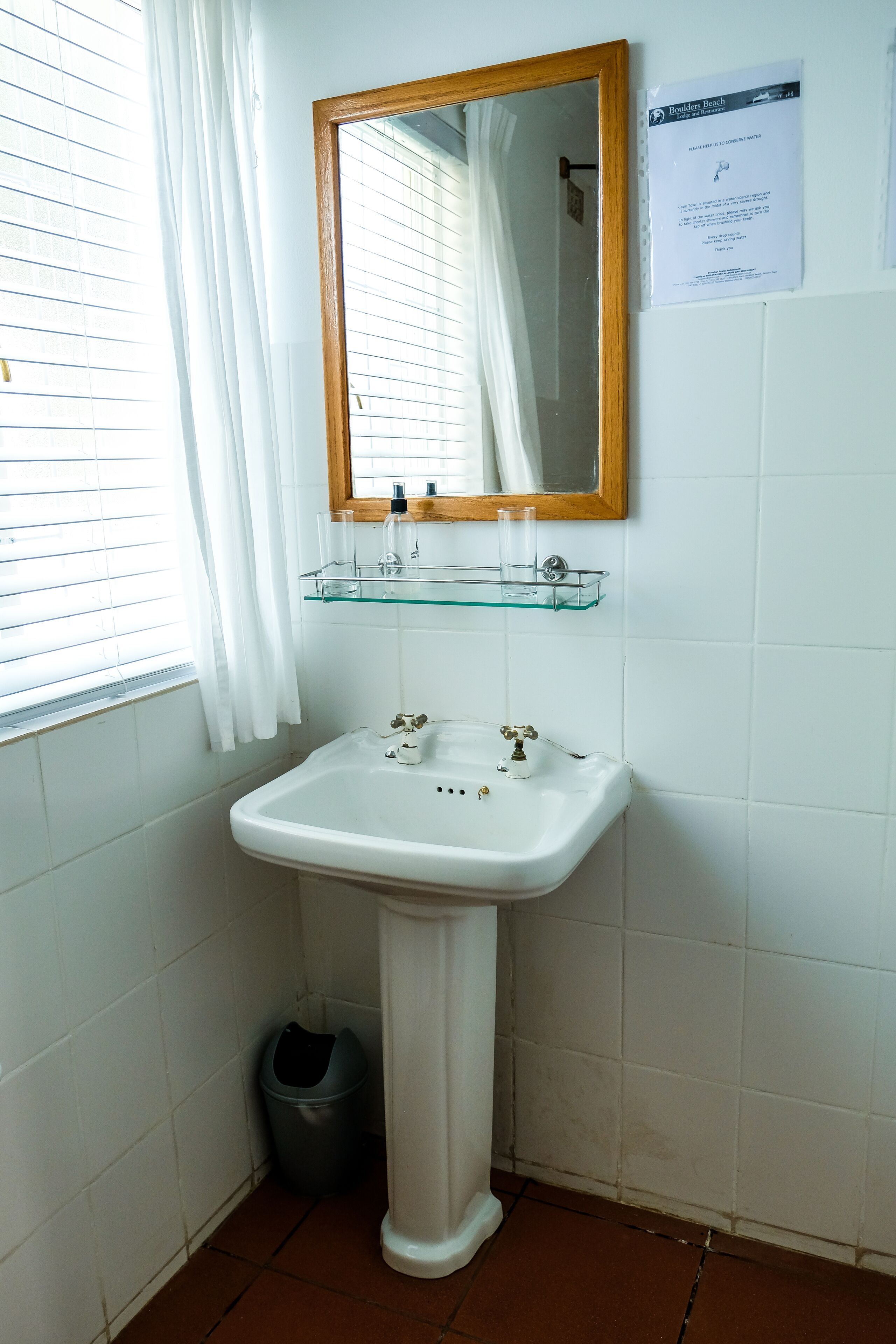 A bathroom with a white sink, a mirror, and a glass shelf.