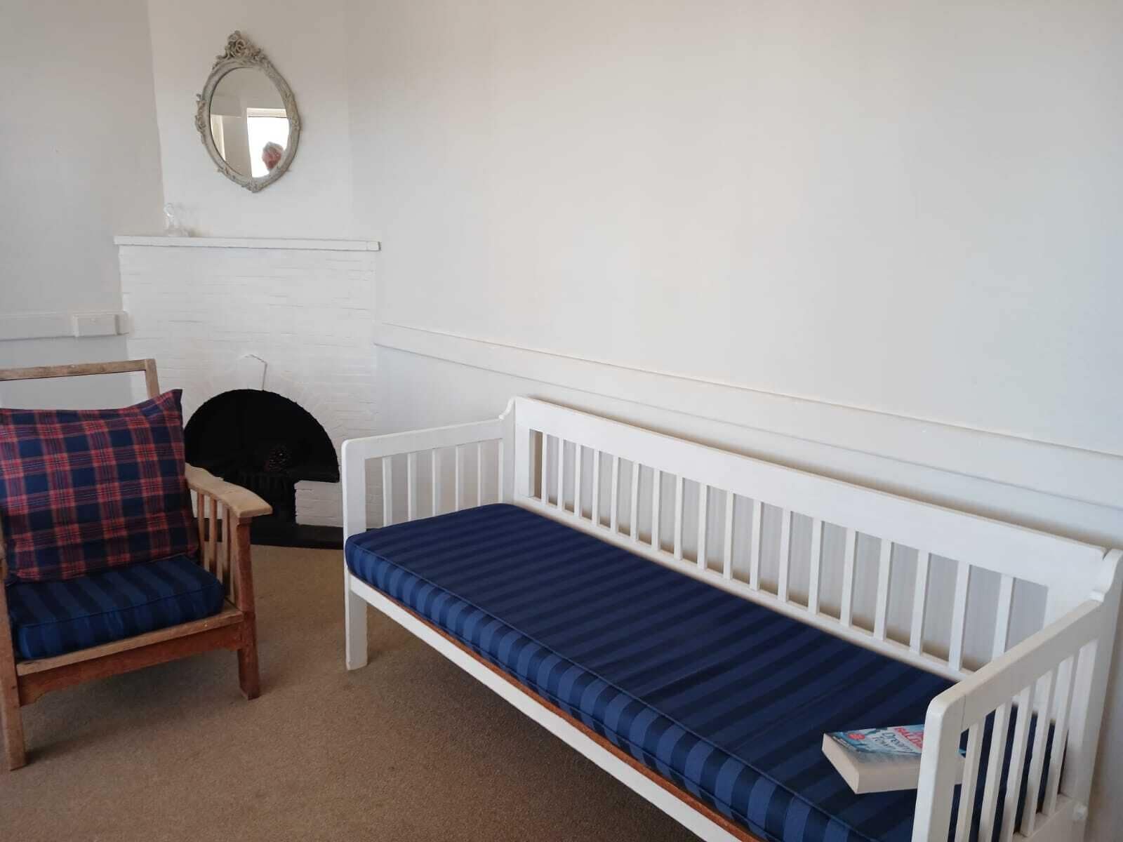 A room with a white bench, a wooden chair with a plaid cushion, and a mirror on the wall.