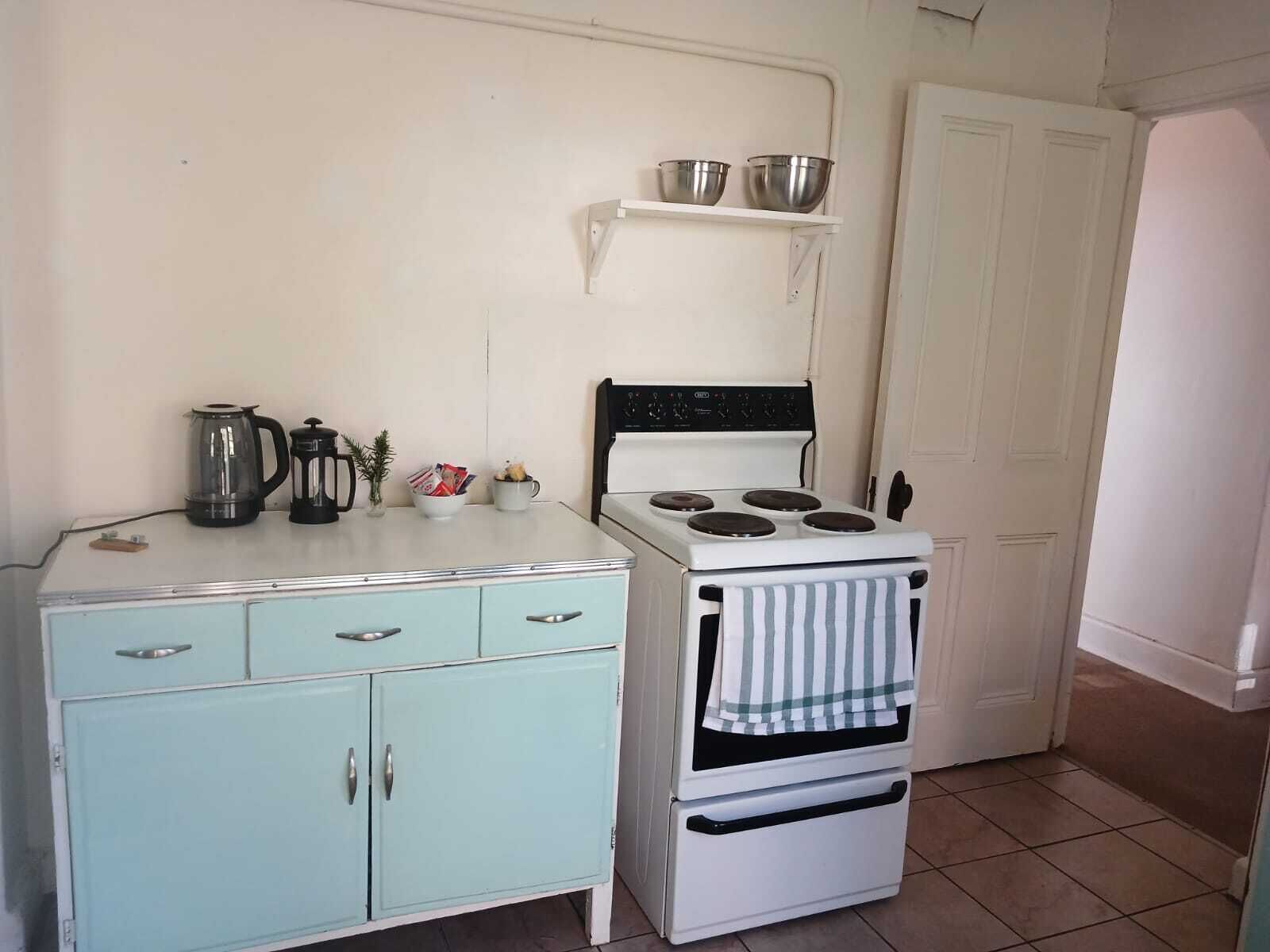 A compact kitchen with a vintage stove, a small cabinet, and a shelf above the stove.