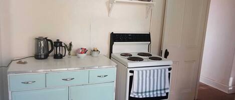 A compact kitchen with a vintage stove, a small cabinet, and a shelf above the stove.
