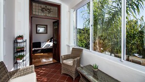 A sunlit room with wicker furniture, a large window with a view of greenery, and a door leading to another room. - Carmichael Guesthouse (Rosebank)