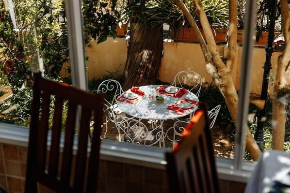 A round table with a white tablecloth and red napkins, set outdoors with metal chairs. - Carmichael Guesthouse (Rosebank)