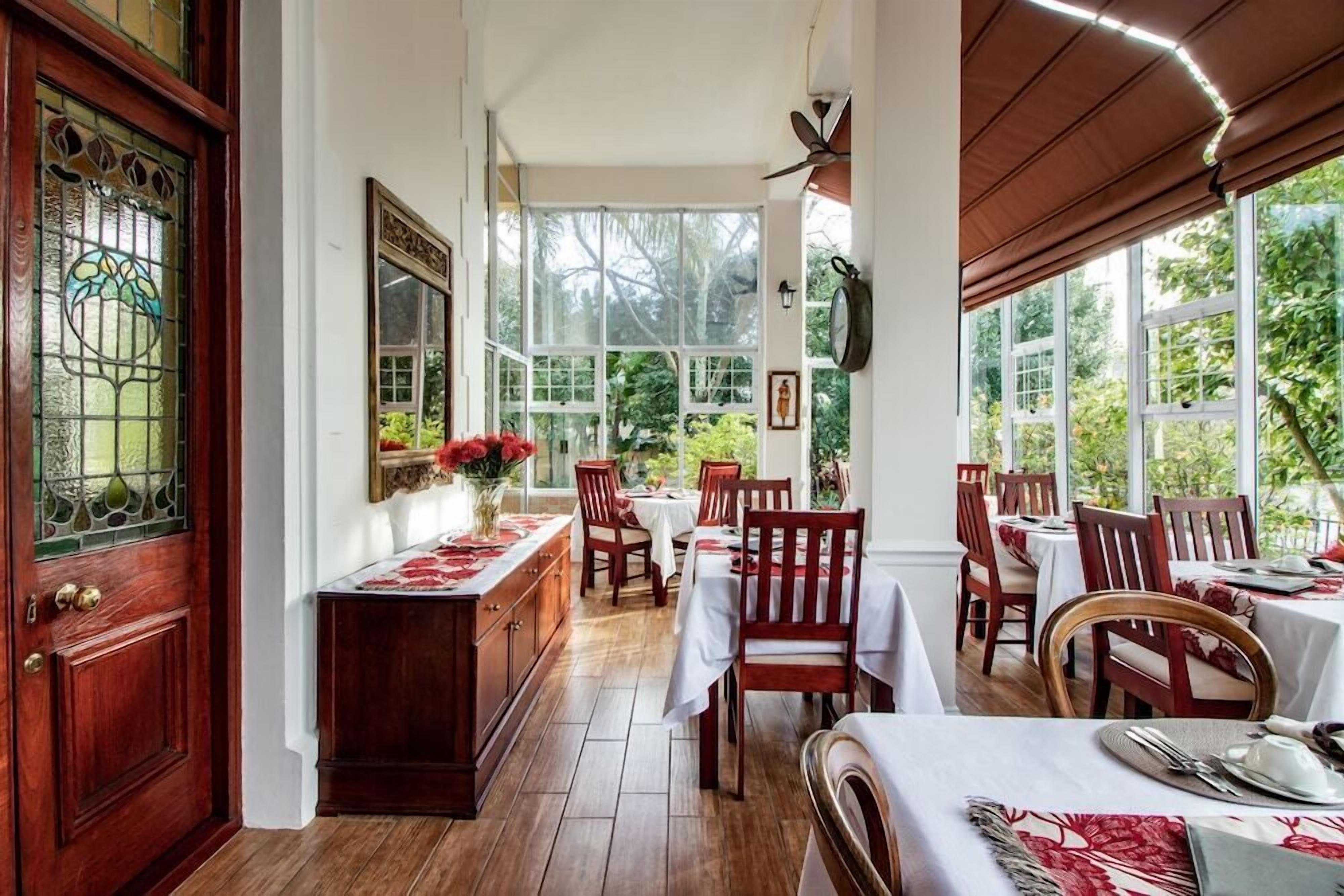 A dining area with wooden tables and chairs, large windows, and a decorative door.