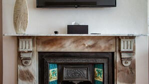 A fireplace with a decorative screen, a flat-screen TV mounted above it, and a vase on the mantel. - Carmichael Guesthouse (Rosebank)