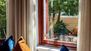 A window with curtains, a view of greenery outside, and a glimpse of a wooden table and chairs. - Carmichael Guesthouse (Rosebank)