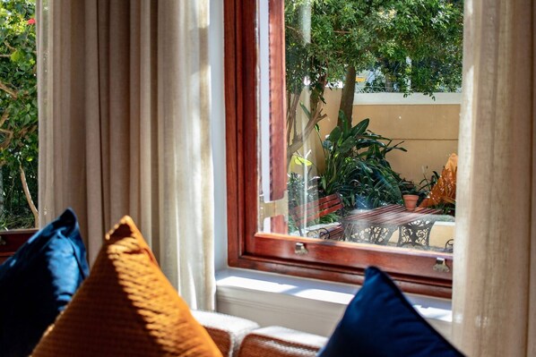 A window with curtains, a view of greenery outside, and a glimpse of a wooden table and chairs. - Carmichael Guesthouse (Rosebank)