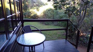 Une terrasse dotée d’une table et de chaises, donnant sur un jardin où poussent différentes plantes et arbres.