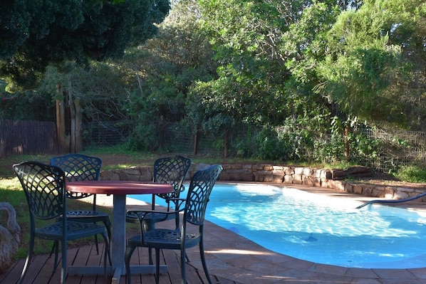 A backyard with a swimming pool, surrounded by a stone wall and a wooden deck. - Woodlands Cottages & Camping (Kenton on Sea)