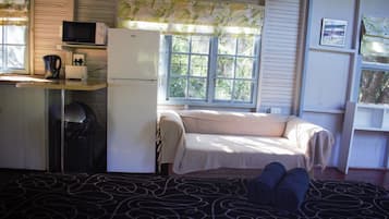 Una habitación pequeña con cama, kitchenette y ventana con cortinas.