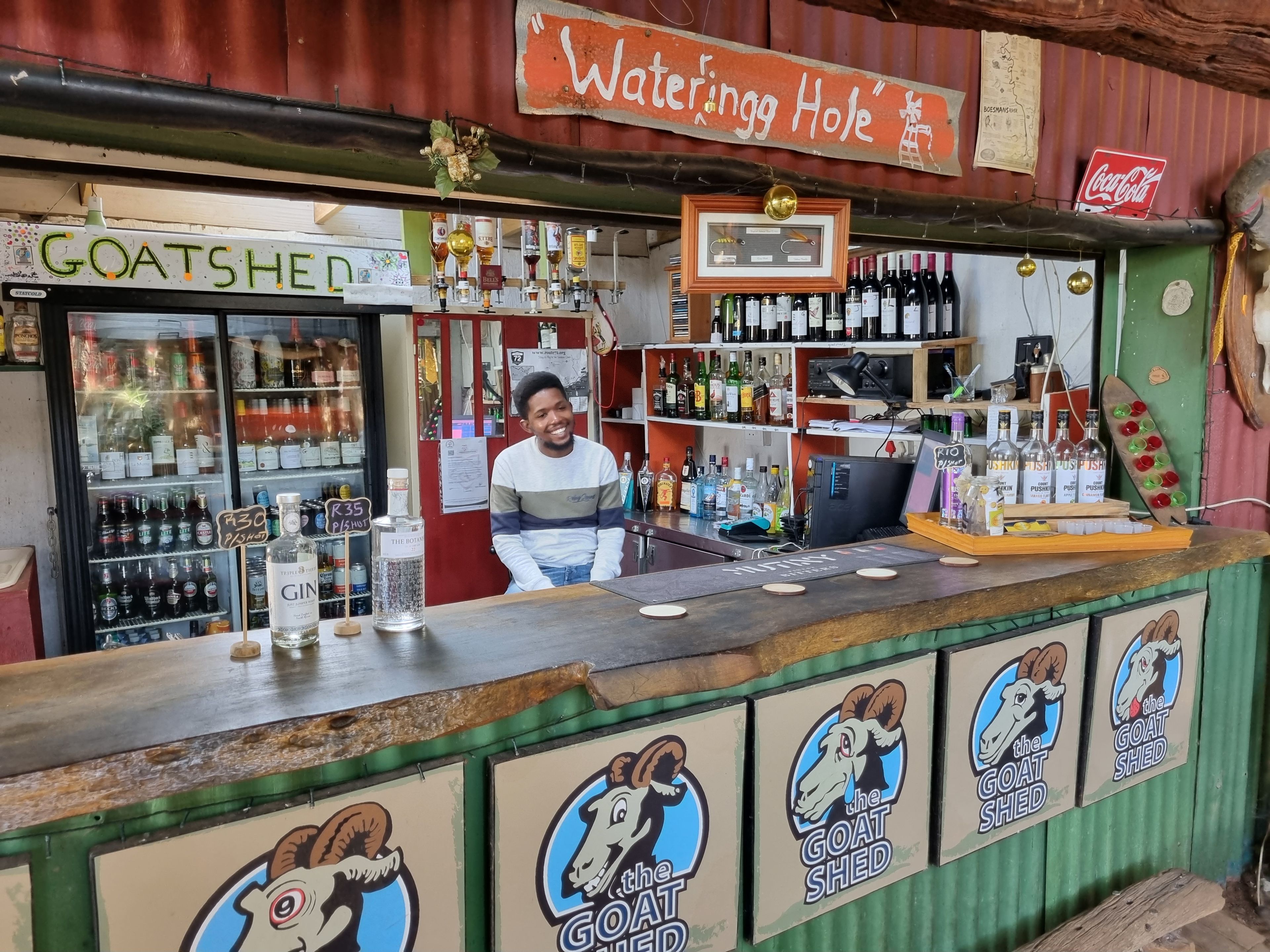 A bar with a goat-themed logo, a Coca-Cola sign, and a variety of liquor bottles.