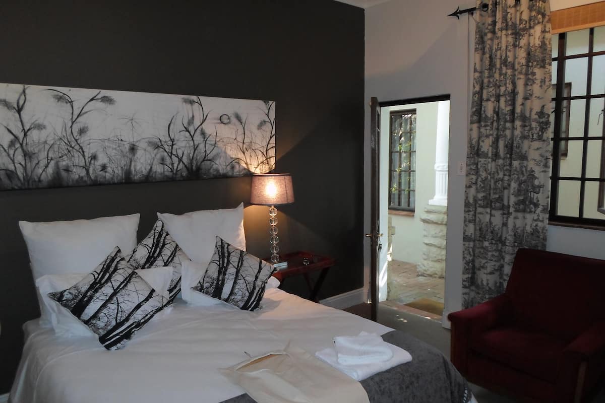 Ein Hotelzimmer mit einem Bett, einem roten Sessel, einer Lampe und Blick ins Freie.