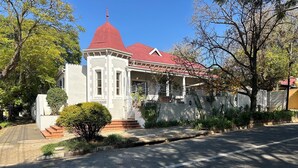 A building with a red roof and white walls, a small garden, and a clear sky. - Melville Turret Guesthouse (Johannesburg)
