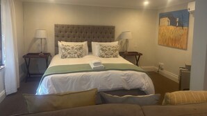 A hotel room with a large bed, two bedside tables with lamps, a painting on the wall, and a sofa in the foreground. - Melville Turret Guesthouse (Johannesburg)