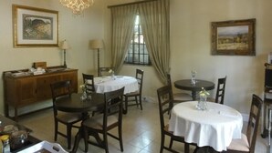 A dining area with two round tables, wooden chairs, a wooden cabinet, and a chandelier. - Melville Turret Guesthouse (Johannesburg)