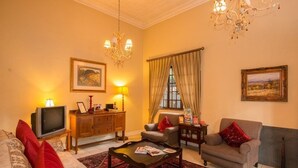 A living room with a sofa, armchair, coffee table, television, and artwork on the walls. - Melville Turret Guesthouse (Johannesburg)