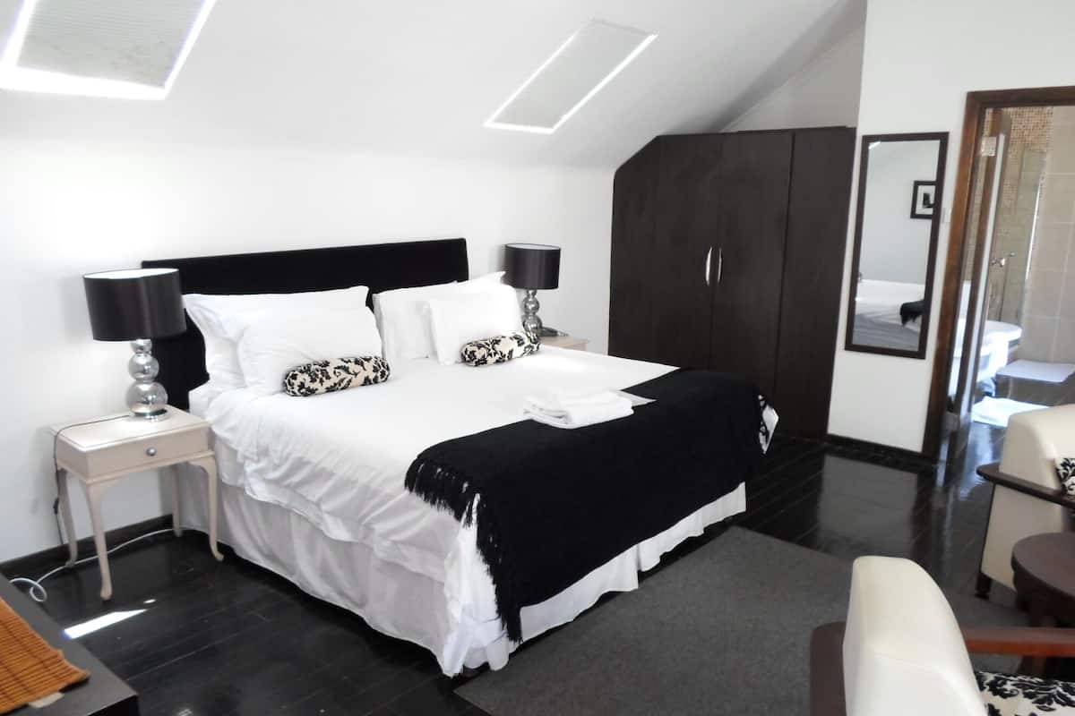 Ein modernes Hotelzimmer mit einem großen Bett, einem Kleiderschrank, einem Schreibtisch mit Lampe und einem Sessel.