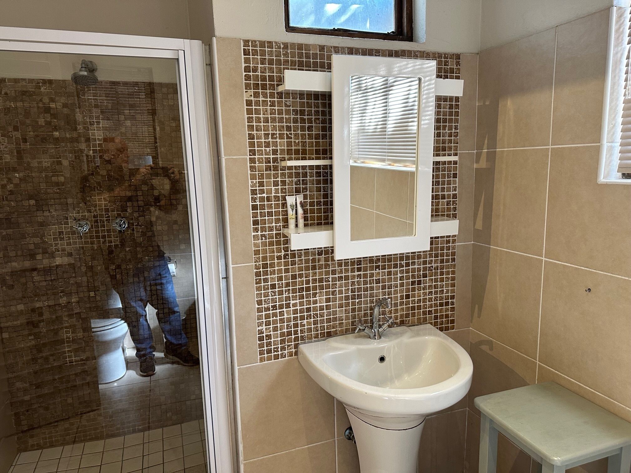 A bathroom with a tiled wall, a sink, a mirror, and a shower.