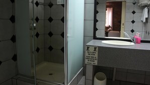 Un baño con ducha de vidrio, un lavabo con espejo y un letrero que indica desechar cualquier residuo en un contenedor.