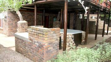 A rustic outdoor area with a brick structure, a stone bench, and a covered wooden deck.