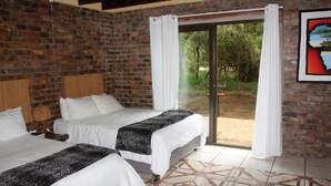Una habitación con dos camas, una pared de ladrillo, una puerta de vidrio que da al exterior y un piso con diseño.