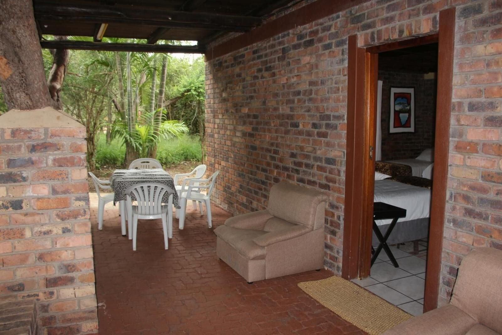 Una habitación con pared de ladrillo, una cama, una mesita con sillas y vistas al exterior con vegetación.