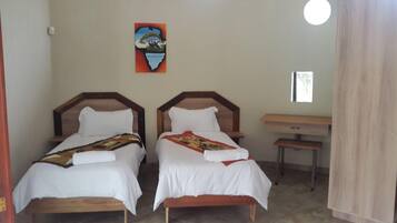 A room with two wooden beds, a small table, a bench, and a painting on the wall.