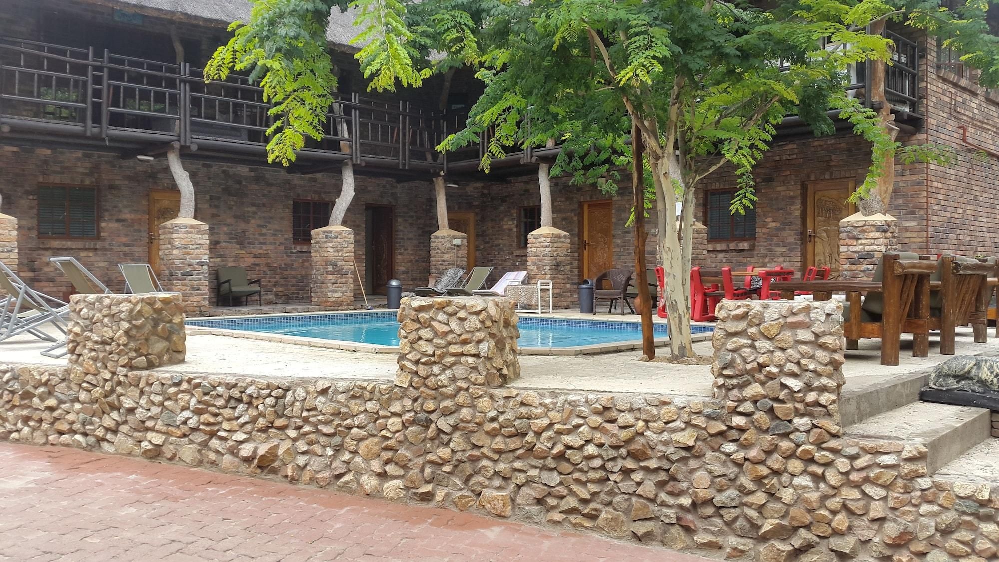 A pool area with stone walls, lounge chairs, and a brick building in the background.