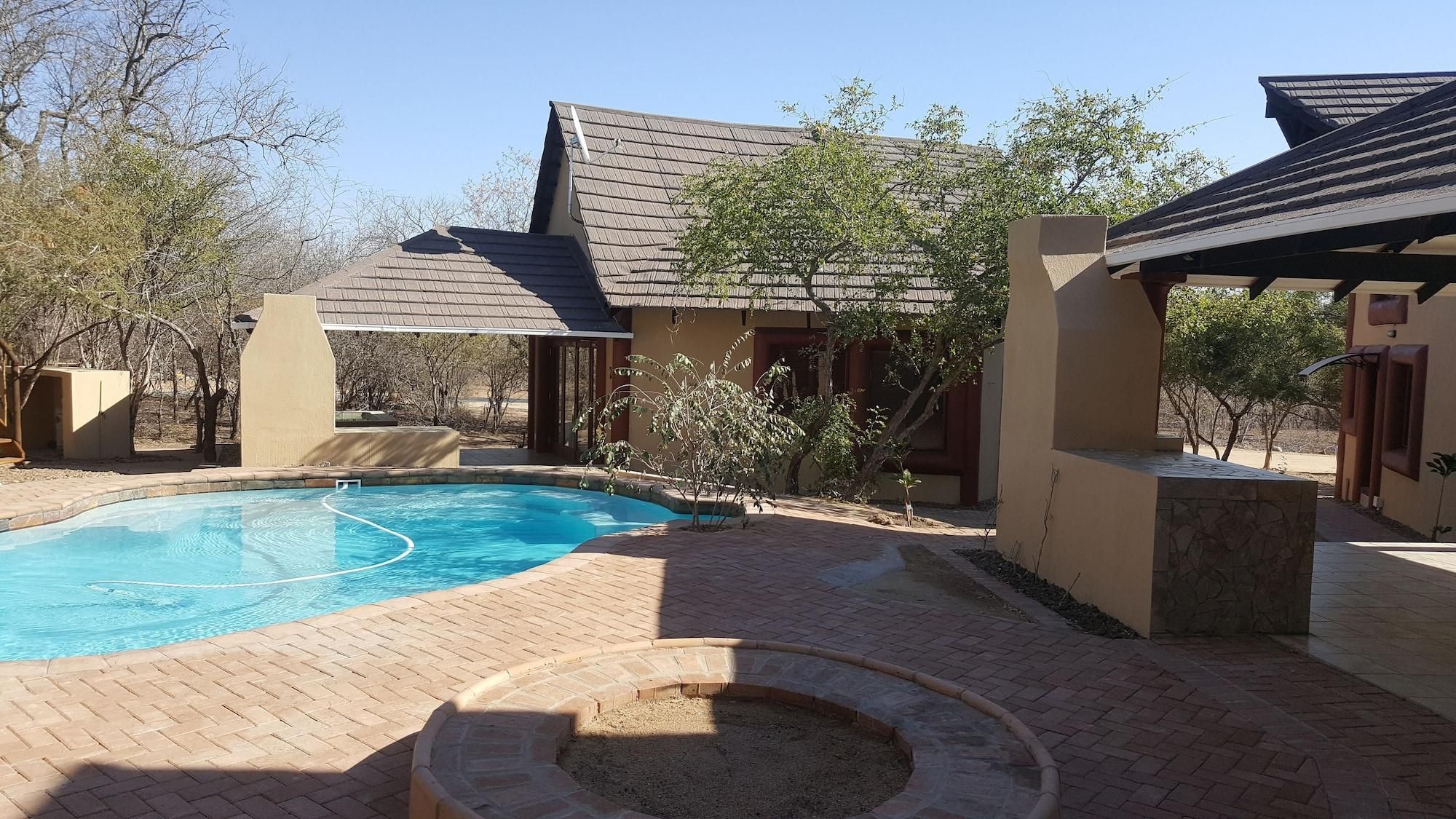 A swimming pool with a brick deck, a covered patio area, and a small fire pit.