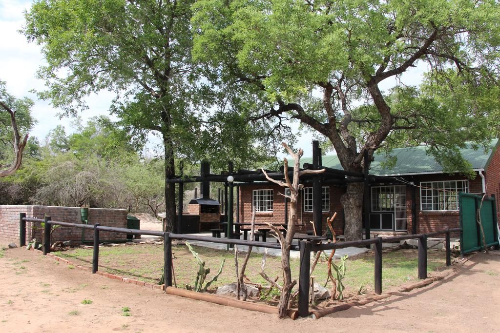 A rustic building with a brick exterior, large windows, and a fenced outdoor area with trees and a bench.