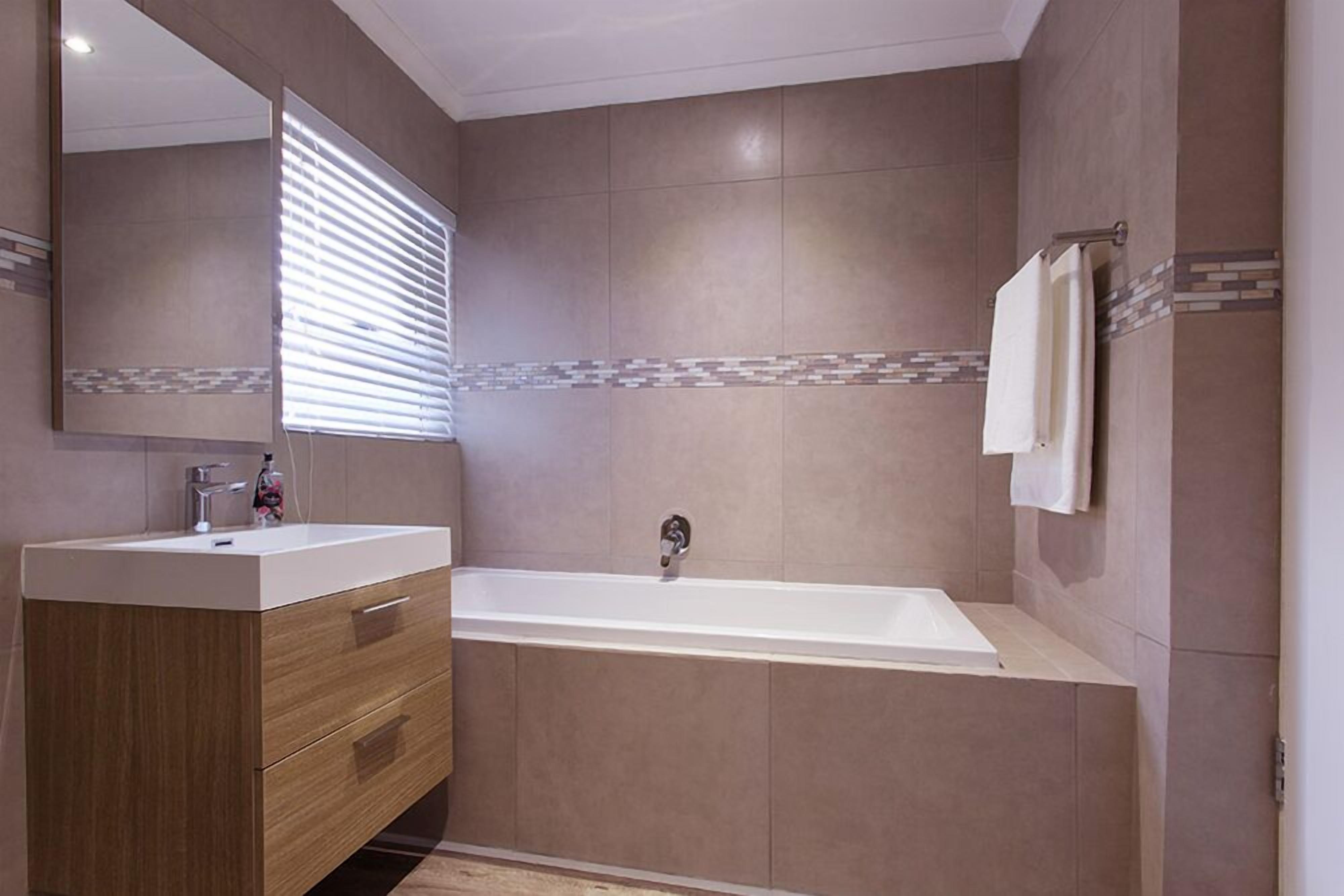 Une salle de bain moderne avec un meuble-lavabo en bois, une grande baignoire et un miroir orné d’une bordure de carreaux décoratifs.