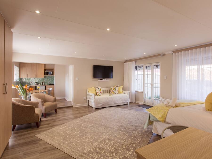 A modern hotel room with a sofa, a bed, a TV, and a kitchen area in the background.